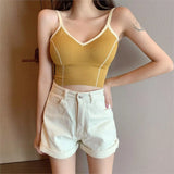 Person wearing a mustard yellow tank top and white shorts against a neutral background