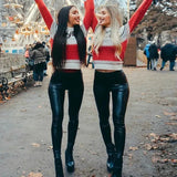 Two women in matching red and white sweaters with black leather pants standing in a park.