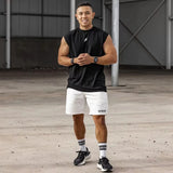 Man wearing a black sleeveless shirt and white shorts standing on a wooden floor.