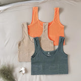 Three ribbed tank tops in orange, beige, and blue on a light gray surface.
