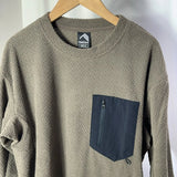 Brown textured sweater with a navy pocket on a hanger against a white background