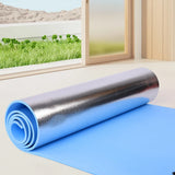 Roll of blue and silver insulation material on a floor with a window view of greenery.