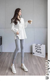 Woman in white blouse and gray leggings holding a coffee cup in a room with 'Paris' sign.
